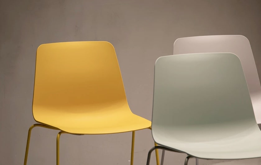 A gold-colored chair and a silver chair behind a steel-blue chair, all of the same minimalistic design, facing forwards in a triangular formation