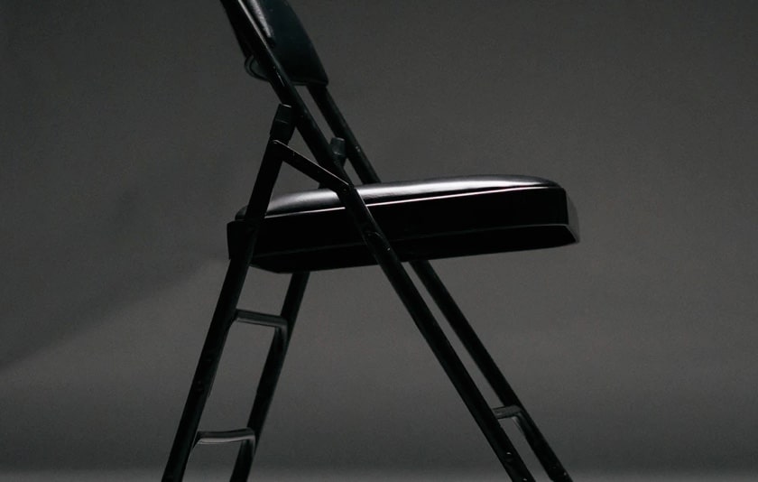 A side-on view of a black, collapsible chair with a cushioned seat and back support