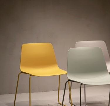 A gold-colored chair and a silver chair behind a steel-blue chair, all of the same minimalistic design, facing forwards in a triangular formation