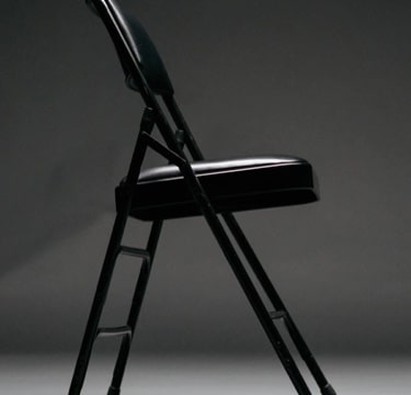 A side-on view of a black, collapsible chair with a cushioned seat and back support